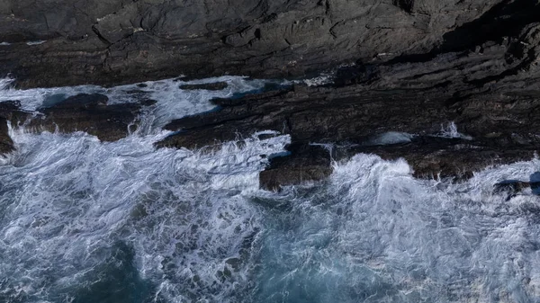 Kuvvetli dalgalarla kayalıklara çarpan kayalık kıyı şeridi berrak bir gökyüzü altında, derin mavi okyanus ve çorak kara arasındaki zıtlığı gözler önüne seriyor..