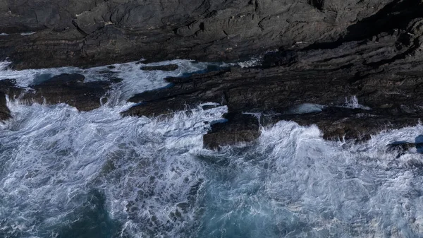 Kuvvetli dalgalarla kayalıklara çarpan kayalık kıyı şeridi berrak bir gökyüzü altında, derin mavi okyanus ve çorak kara arasındaki zıtlığı gözler önüne seriyor..