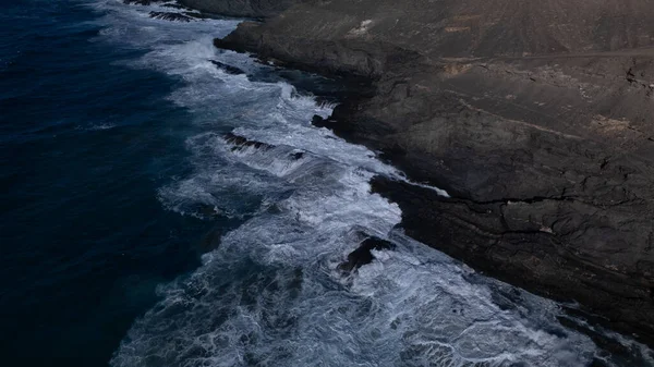 Kuvvetli dalgalarla kayalıklara çarpan kayalık kıyı şeridi berrak bir gökyüzü altında, derin mavi okyanus ve çorak kara arasındaki zıtlığı gözler önüne seriyor..