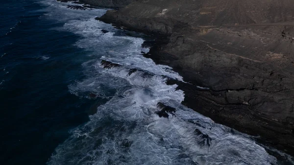 Kuvvetli dalgalarla kayalıklara çarpan kayalık kıyı şeridi berrak bir gökyüzü altında, derin mavi okyanus ve çorak kara arasındaki zıtlığı gözler önüne seriyor..