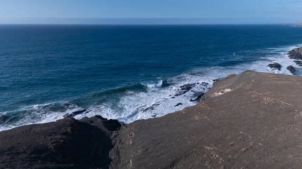 Kuvvetli dalgalarla kayalıklara çarpan kayalık kıyı şeridi berrak bir gökyüzü altında, derin mavi okyanus ve çorak kara arasındaki zıtlığı gözler önüne seriyor..
