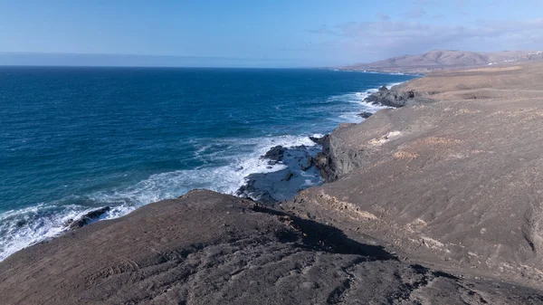Kuvvetli dalgalarla kayalıklara çarpan kayalık kıyı şeridi berrak bir gökyüzü altında, derin mavi okyanus ve çorak kara arasındaki zıtlığı gözler önüne seriyor..