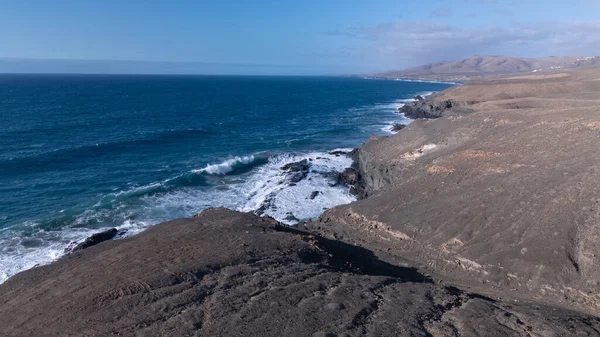 Kuvvetli dalgalarla kayalıklara çarpan kayalık kıyı şeridi berrak bir gökyüzü altında, derin mavi okyanus ve çorak kara arasındaki zıtlığı gözler önüne seriyor..
