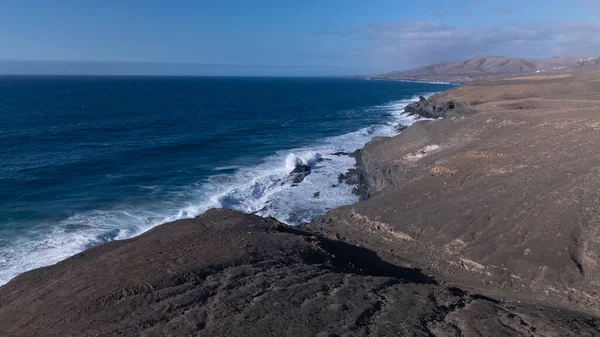 Kuvvetli dalgalarla kayalıklara çarpan kayalık kıyı şeridi berrak bir gökyüzü altında, derin mavi okyanus ve çorak kara arasındaki zıtlığı gözler önüne seriyor..