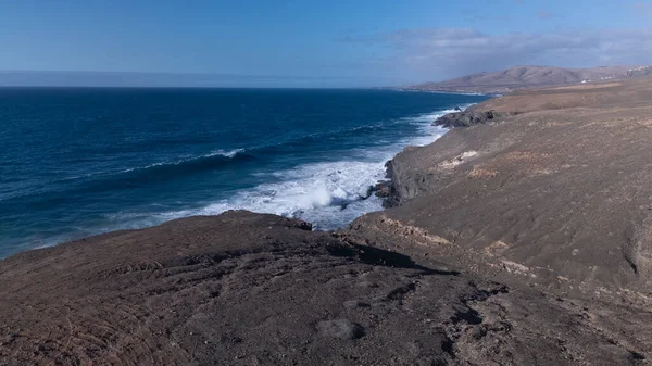 Kuvvetli dalgalarla kayalıklara çarpan kayalık kıyı şeridi berrak bir gökyüzü altında, derin mavi okyanus ve çorak kara arasındaki zıtlığı gözler önüne seriyor..