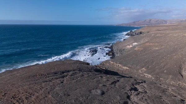 Kuvvetli dalgalarla kayalıklara çarpan kayalık kıyı şeridi berrak bir gökyüzü altında, derin mavi okyanus ve çorak kara arasındaki zıtlığı gözler önüne seriyor..
