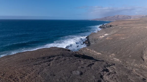 Kuvvetli dalgalarla kayalıklara çarpan kayalık kıyı şeridi berrak bir gökyüzü altında, derin mavi okyanus ve çorak kara arasındaki zıtlığı gözler önüne seriyor..