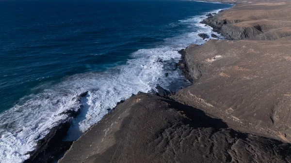 Kuvvetli dalgalarla kayalıklara çarpan kayalık kıyı şeridi berrak bir gökyüzü altında, derin mavi okyanus ve çorak kara arasındaki zıtlığı gözler önüne seriyor..