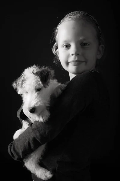 Cute young girl and her wire fox terrier puppy in the studio in monochrome