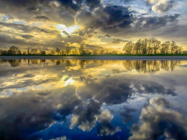 Molnigt himmel i ett landsbygdslandskap reflekteras i en pöl — Stockfoto