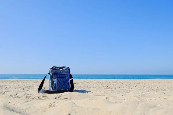 Blue denim bag with black strap on sandy beach — Stock Photo, Image