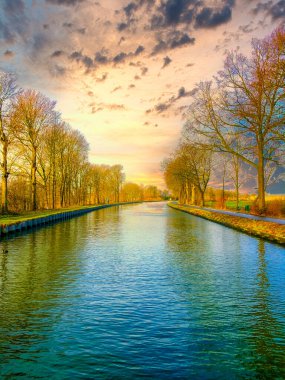 Ağaçlarla çevrili bir su kütlesinin üzerinde dramatik bir gün batımı.