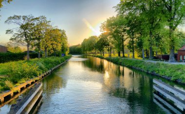 Ağaçlarla çevrili bir su kütlesinin üzerinde dramatik bir gün batımı.