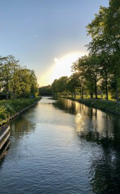 Ağaçlarla çevrili bir su kütlesinin üzerinde dramatik bir gün batımı.
