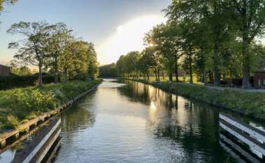 Ağaçlarla çevrili bir su kütlesinin üzerinde dramatik bir gün batımı.