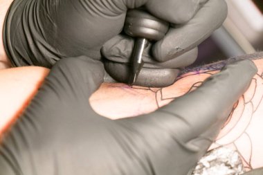 Erkek bir dövme ustası müşterisiyle çalışıyor.