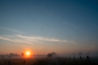 Sakin ve huzurlu bir gün doğumu sisli bir alanı güzelce aydınlatıyor, doğanın güzelliğini özetliyor.