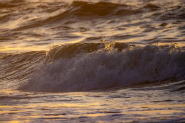 Okyanus dalgaları, gün batımının sıcak renkleriyle aydınlanarak, huzurlu ve huzurlu bir manzara yaratıyor.