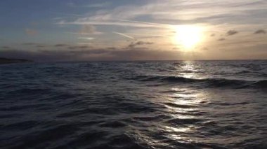 Güneş doğarken nefes kesen güzel okyanus manzarası, yumuşak dalgalar ve sakin bir atmosfer sergiliyor.