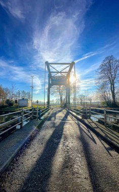 Parlak güneş ışığı ve dramatik gölgeleriyle mavi gökyüzünün altında çarpıcı bir köprü nefes kesici bir manzara yaratır.