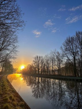 Şaşırtıcı derecede güzel bir gün doğumu bereketli ağaçlarla çevrili huzurlu ve huzurlu bir nehri aydınlatır.