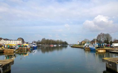 Renkli teknelerle sakin bir liman sahnesi ve berrak mavi gökyüzünün altındaki sakin sularda yansımaları.