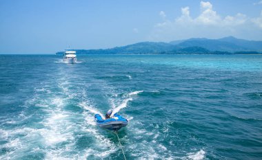 Beyaz gemi ve denizde bir tekne. Beyaz köpüklü dalgalarda halatta şişme bot. Tayland. Andaman Denizi.