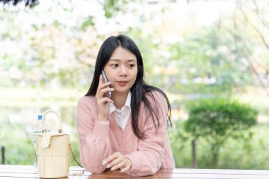 Tayvan 'ın Taipei şehrinde bir parkta 20' li yaşlarda genç bir Tayvanlı kadın bir bankta oturuyor ve akıllı telefonuyla konuşuyor.