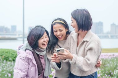 Tayvanlı bir kadının ailesi, Tayvan 'ın Taipei şehrinde nehir kenarındaki büyük bir parkta akıllı telefonuyla gülüp hatıra fotoğrafı çekiyor. 