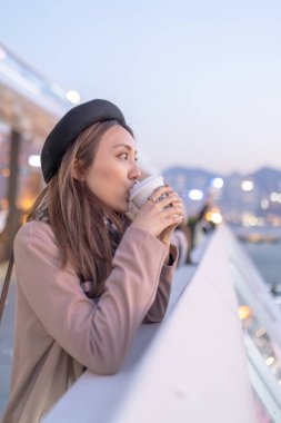 20 'li yaşlarda mini etekli genç bir Çinli kadın Hong Kong Adası' ndaki deniz kenarında bir grup gökdelene bakıyor.