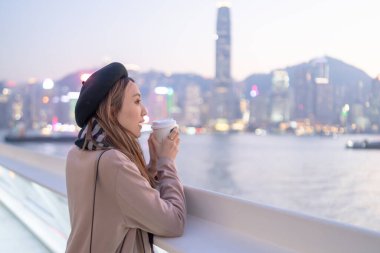 20 'li yaşlarda mini etekli genç bir Çinli kadın Hong Kong Adası' ndaki deniz kenarında bir grup gökdelene bakıyor.