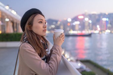 20 'li yaşlarda mini etekli genç bir Çinli kadın Hong Kong Adası' ndaki deniz kenarında bir grup gökdelene bakıyor.