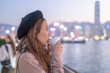 20 'li yaşlarda mini etekli genç bir Çinli kadın Hong Kong Adası' ndaki deniz kenarında bir grup gökdelene bakıyor.
