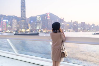 20 'li yaşlarda mini etekli genç bir Çinli kadın Hong Kong Adası' ndaki deniz kenarında bir grup gökdelene bakıyor.