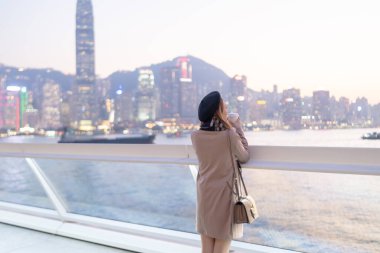 20 'li yaşlarda mini etekli genç bir Çinli kadın Hong Kong Adası' ndaki deniz kenarında bir grup gökdelene bakıyor.