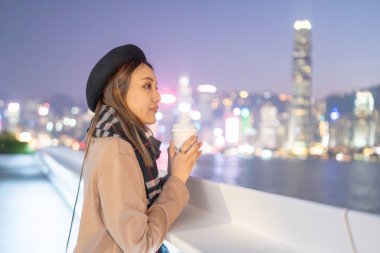 20 'li yaşlarda mini etekli genç bir Çinli kadın Hong Kong Adası' ndaki deniz kenarında bir grup gökdelene bakıyor.