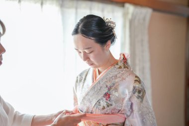 Kimonolu bir kadına kıyafetlerini değiştirmesi için başka bir kadın yardım ediyor. Sahne samimi ve iki kadın arasında bir ilgi ve destek hissi uyandırıyor.