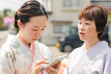Kimonolu iki kadın cep telefonuna bakıyor. İçlerinden biri telefonu elinde tutuyor.
