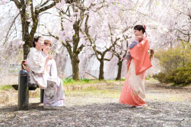 Geleneksel Japon elbiseli bir grup kadın bir parkta bir bankta oturuyorlar. Kadınlardan biri bir bebek tutuyor. Huzurlu ve huzurlu bir sahne. Kadınlar birbirlerine eşlik ediyor.