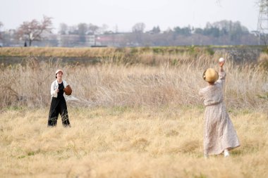 Bir tarlada beyzbol oynayan iki kadın. Biri topu atıyor, diğeri de yakalıyor.