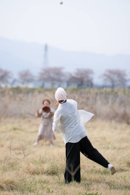 Beyaz gömlekli ve siyah pantolonlu bir adam beyaz elbiseli bir kadınla beyzbol oynuyor.