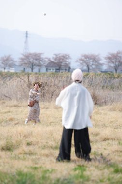 Leopar desenli bir elbise giymiş bir kadın beyzbol topuyla yakalamaca oynuyor. Bir adam onu topu atarken izliyor. Sahne arka planda birkaç ağacın olduğu bir tarlada geçiyor. Sahne neşeli ve neşeli.
