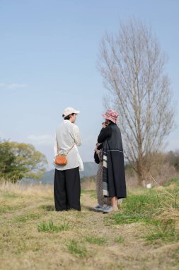 Üç kadın bir tarlada duruyor, biri kırmızı şapka takıyor. Birbirleriyle konuşuyorlar ve içlerinden biri bir bebek tutuyor. Olay yeri sıradan ve dostane.