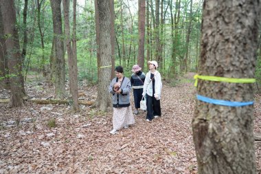 Bir grup kadın ormanda yürüyorlar, içlerinden biri bebek tutuyor. Manzara huzurlu ve huzurlu, kadınlar doğada vakit geçirmekten hoşlanıyor.