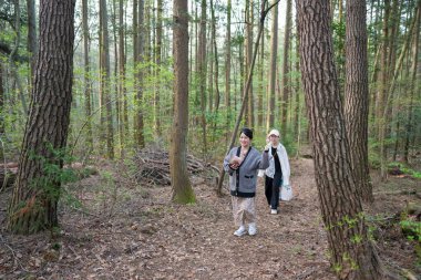Ormanda yürüyen iki kadın. İçlerinden biri bir bebek tutuyor.