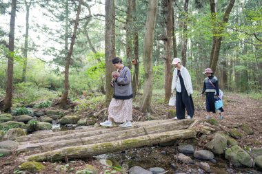 Bir grup insan bir ormandaki köprüden geçiyorlar. Kadınlardan biri bebek taşıyor.