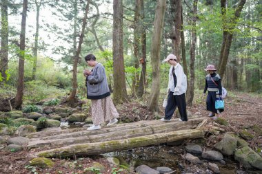 Bir grup kadın bir ormanda köprüden geçiyorlar. Kadınlardan biri bebek taşıyor.