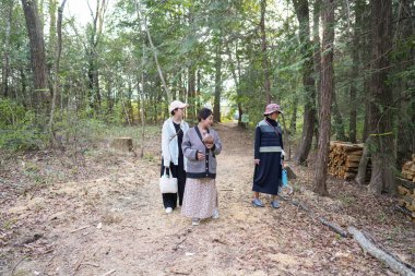 Üç kadın ormanda yürüyor, içlerinden biri bir bebek taşıyor. Manzara huzurlu ve huzurlu, kadınlar doğa yürüyüşünden zevk alıyor.