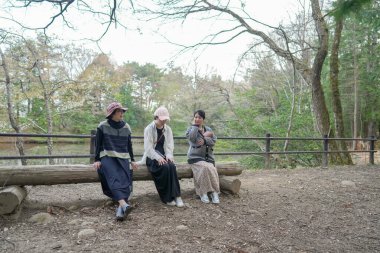 Parktaki bir kütükte üç kadın oturuyor. İçlerinden biri bir bebek tutuyor. Manzara huzurlu ve rahatlatıcı.