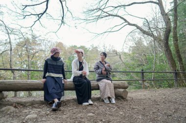 Parktaki bir kütükte üç kadın oturuyor. İçlerinden biri bir bebek tutuyor. Manzara huzurlu ve rahatlatıcı.